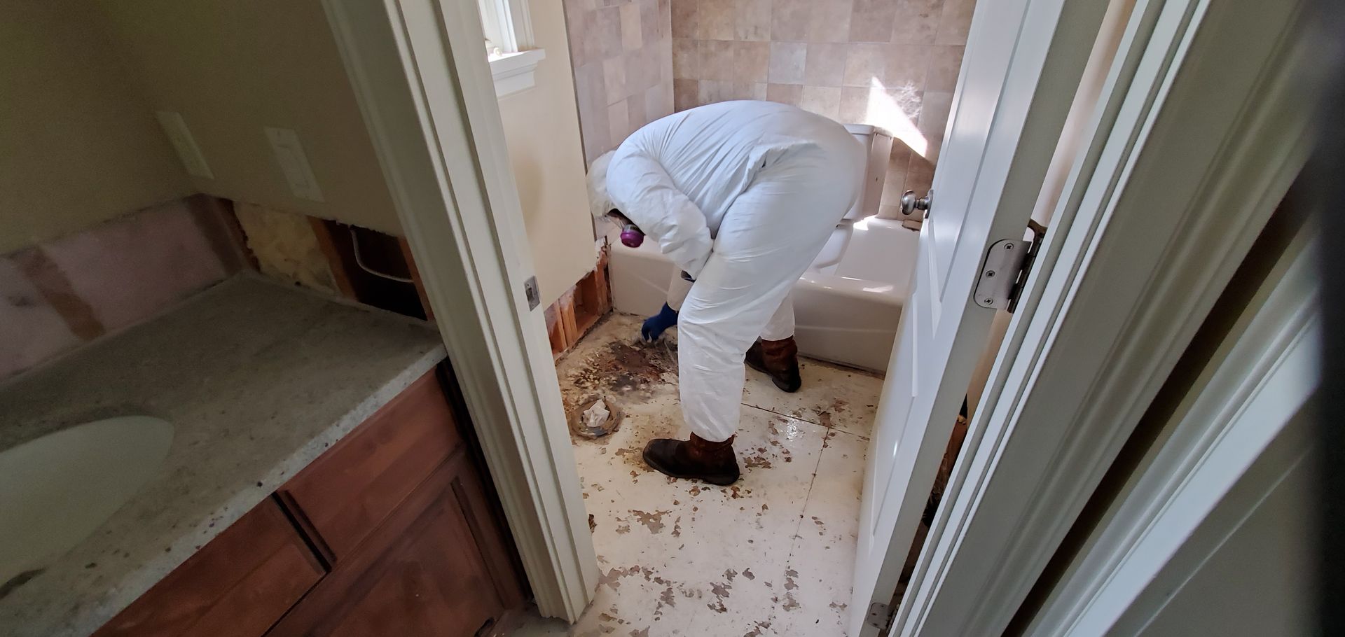 A man in a white suit is cleaning the floor of a bathroom.
