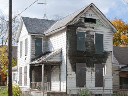 A white house with black shutters on the windows is sitting on the side of the road.