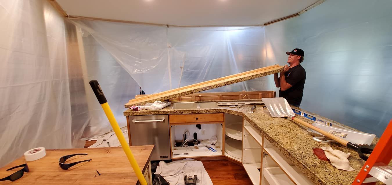 A man is standing in a kitchen holding a piece of wood.