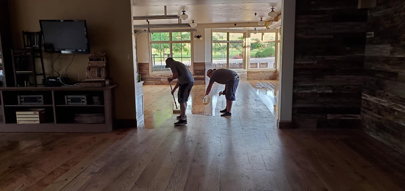 Two men are cleaning a wooden floor in a living room.