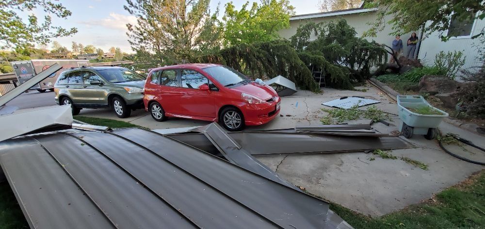 A red car is parked in front of a house that has been damaged by a storm.
