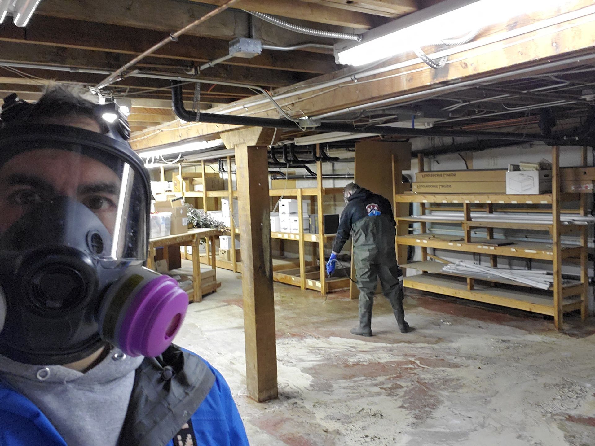 A man wearing a gas mask is standing in a basement.