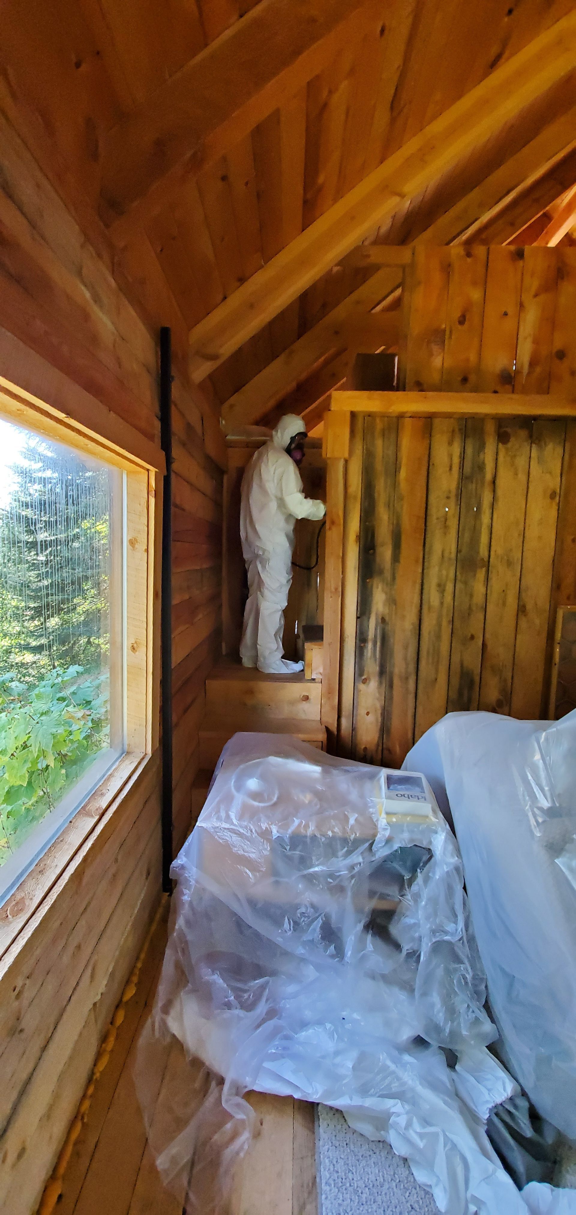 A man in a white suit is working on a wooden wall in a cabin.