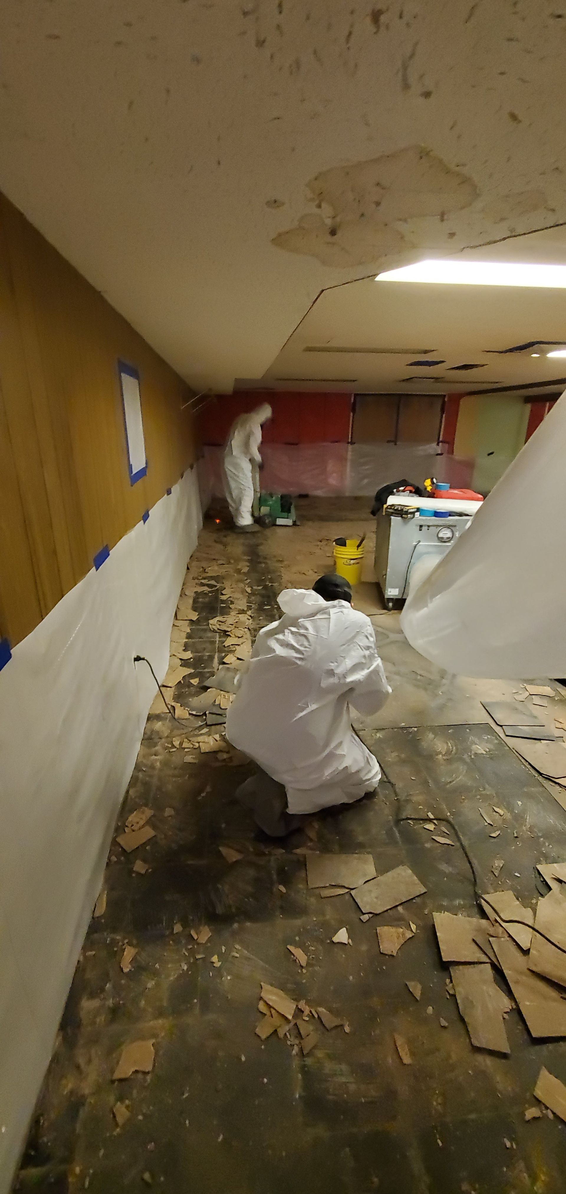 A man in a white suit is kneeling down in a hallway.
