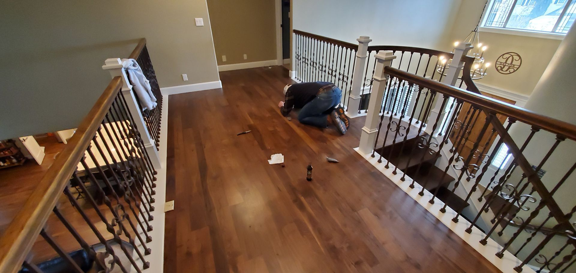 A man is kneeling on a wooden floor next to a staircase.