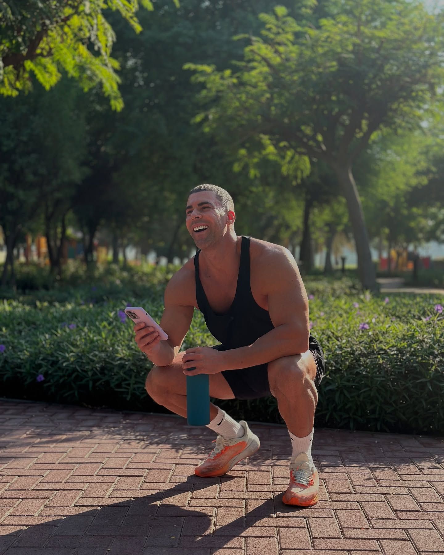 Jay Gardner is squatting down on a brick sidewalk holding a water bottle and a cell phone.