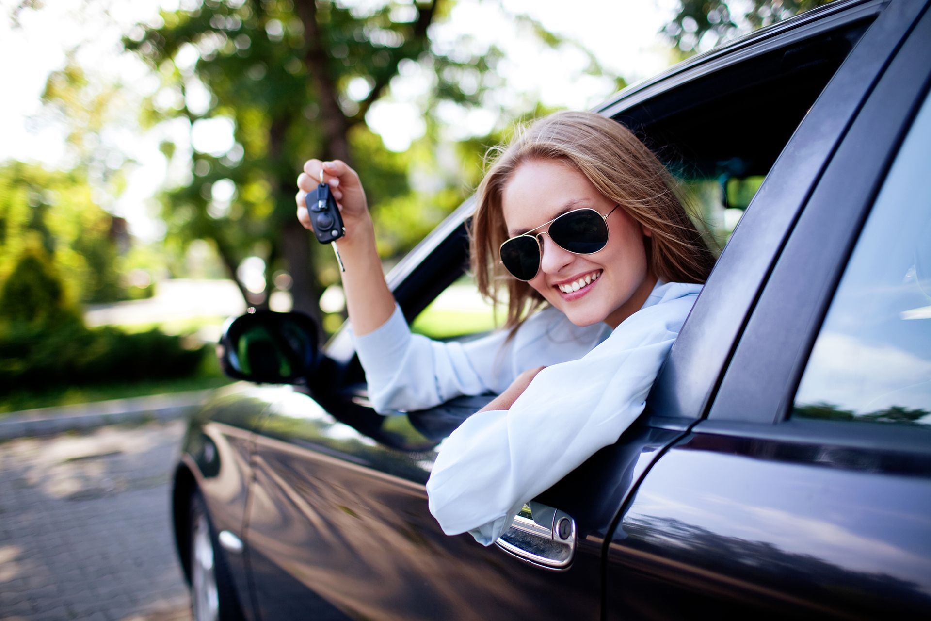 A woman is sitting in a car holding a car key.