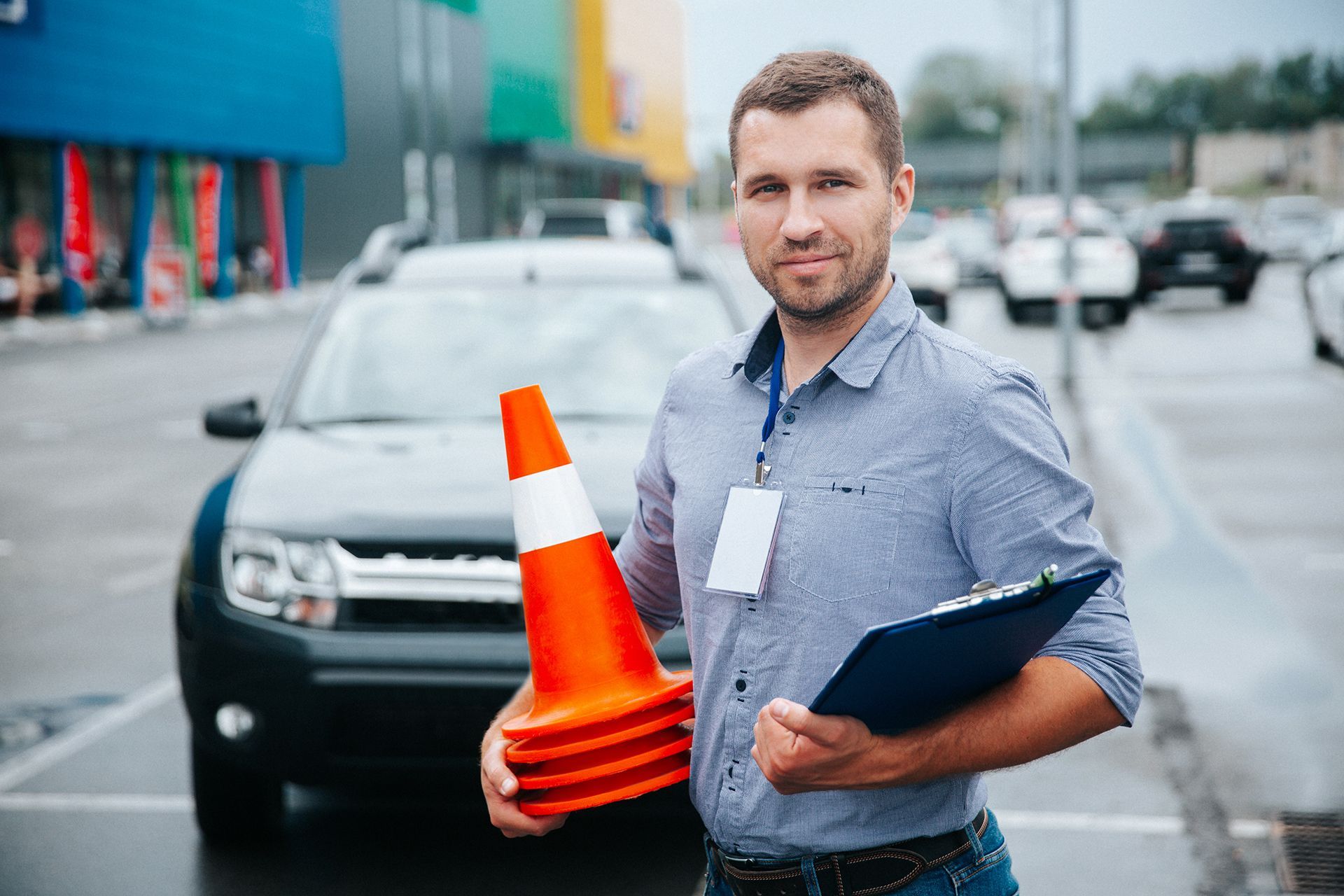 A man is holding a stack of traffic cones and a clipboard in front of a car.