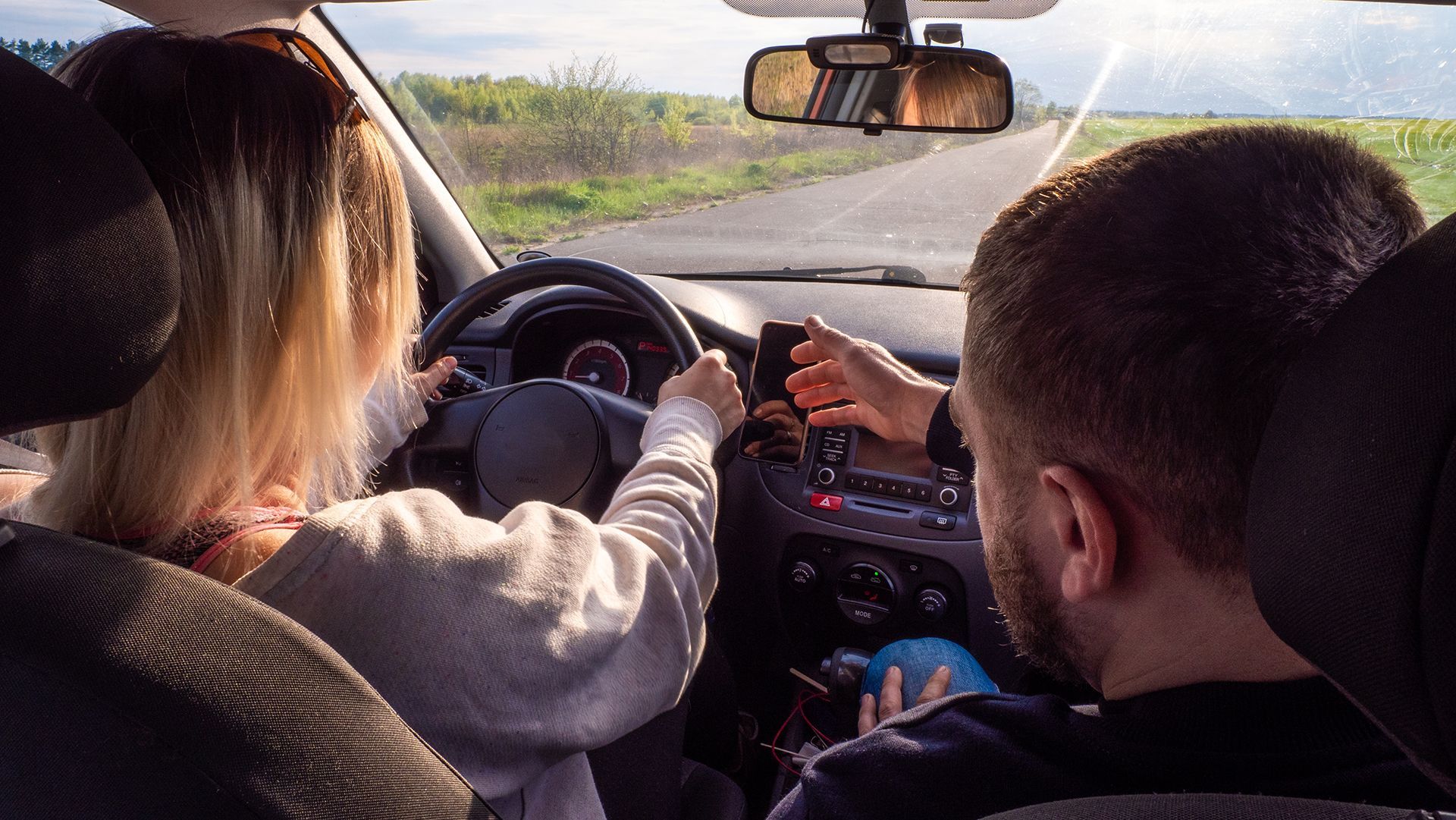 A man and a woman are driving a car and the woman is looking at her phone.