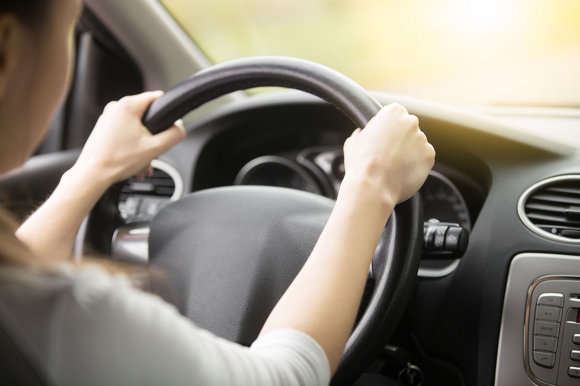 A woman is driving a car with her hands on the steering wheel.