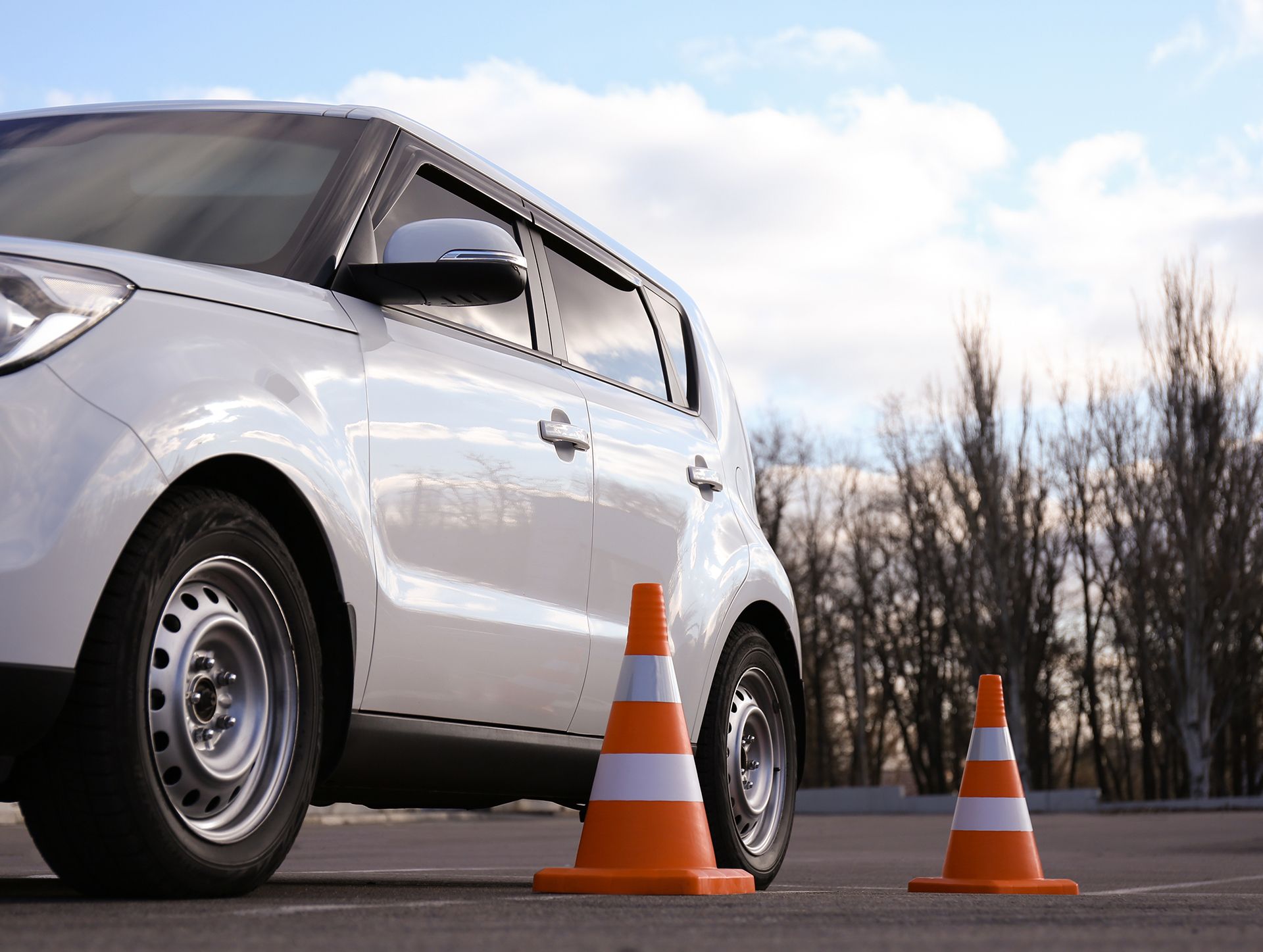 A white car is parked next to two orange and white traffic cones.