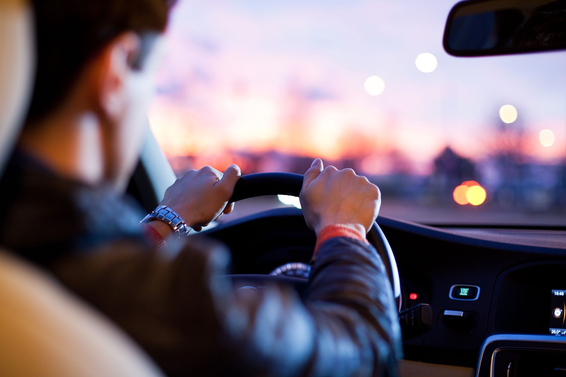 A man is driving a car at night with his hands on the steering wheel.