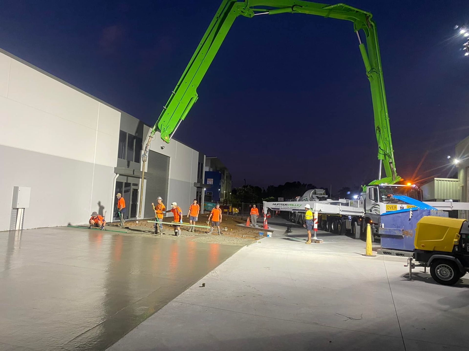 A group of construction workers are working on a concrete driveway in front of a building at night.