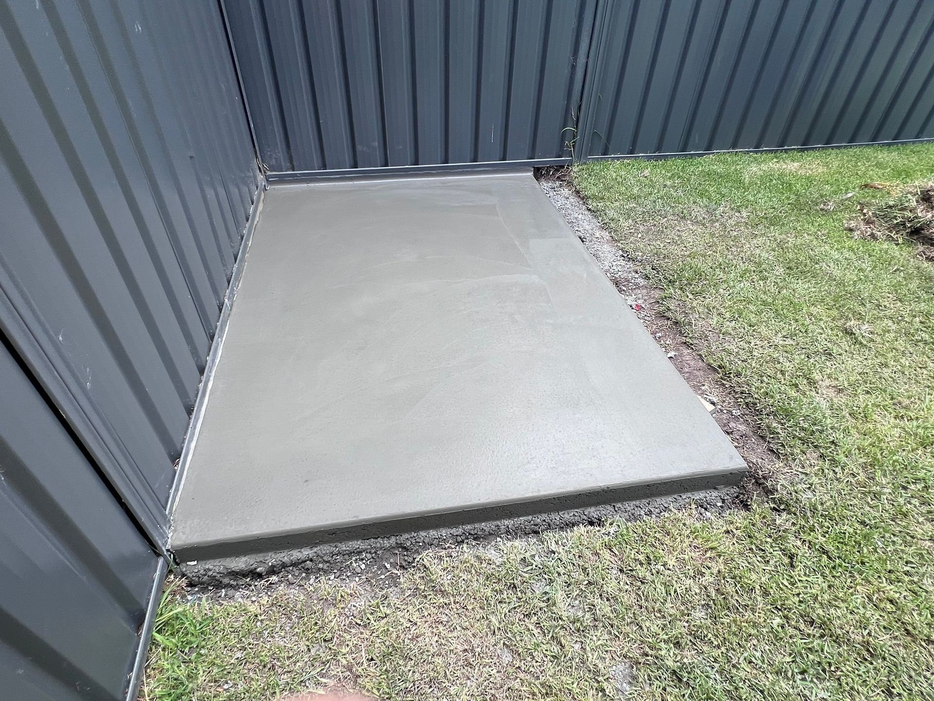 A concrete walkway is being built in the grass next to a fence.