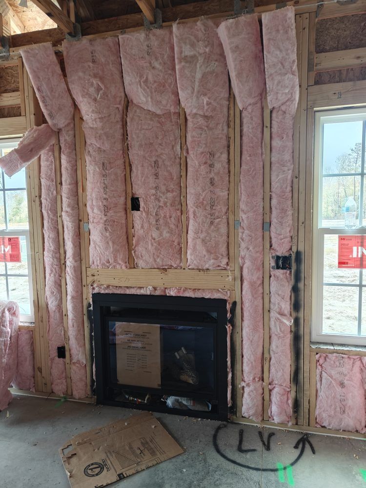 A construction site showing a wall frame with pink fiberglass insulation installed around a black fireplace unit.