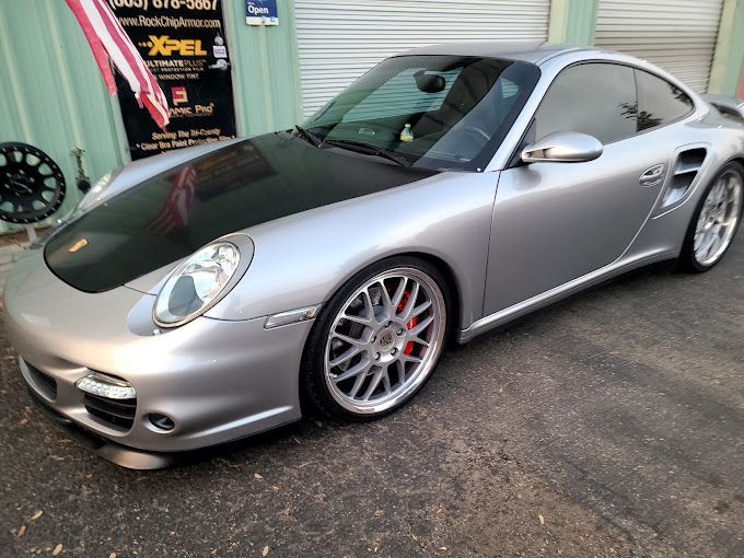 A silver sports car is parked in front of a sign that says xpel