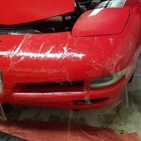 A red sports car with the hood up is sitting in a garage.