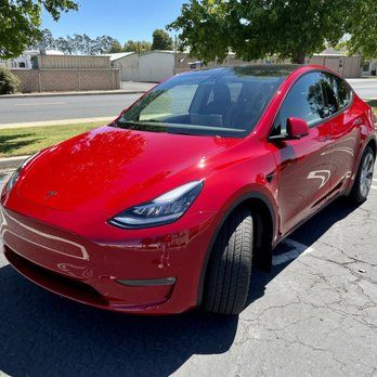 A red tesla model y is parked in a parking lot.