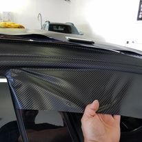 A person is holding a piece of carbon fiber covering the roof of a car.