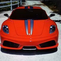 A red sports car with blue stripes is parked on a dirt road.