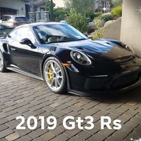 A black porsche 911 gt3 rs is parked on a brick driveway.