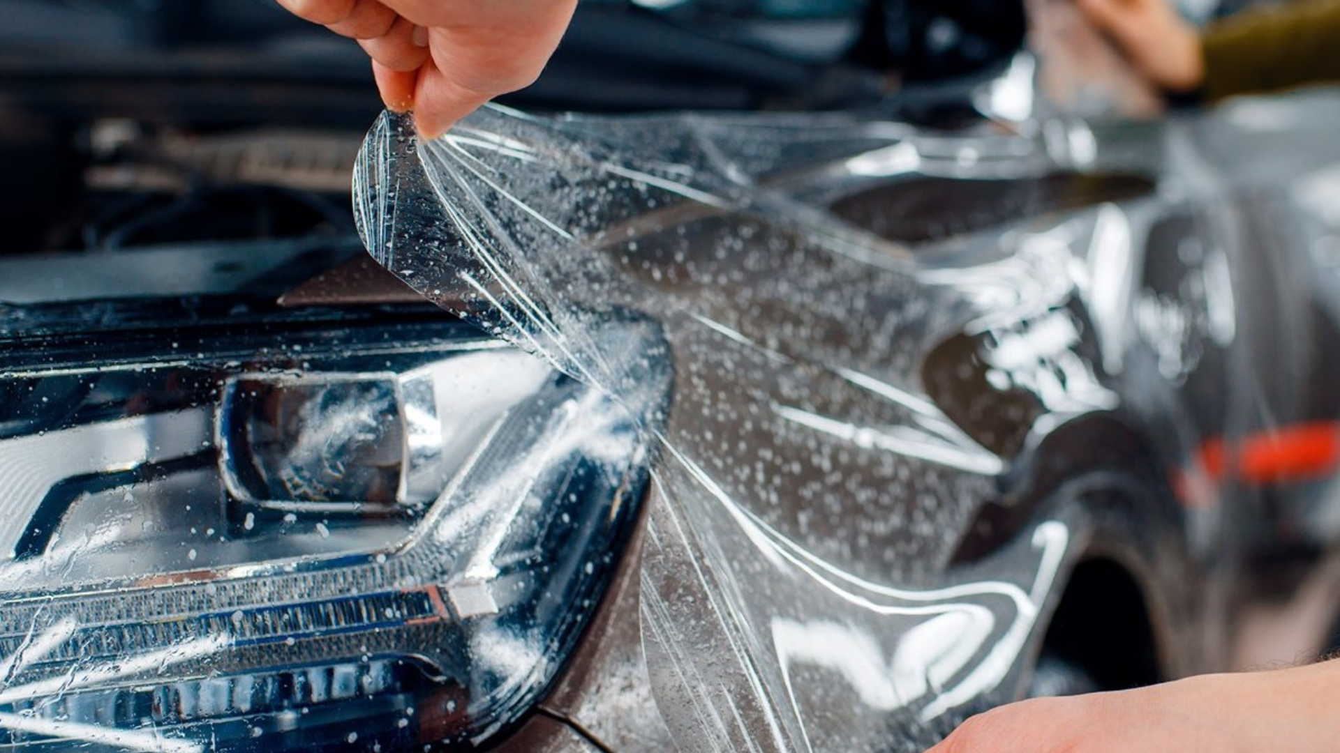 A black car with a damaged hood is parked in front of a garage door.