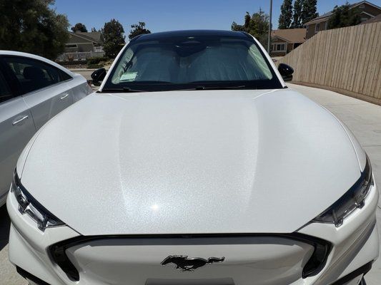 A white ford mustang is parked in a driveway next to a silver car.