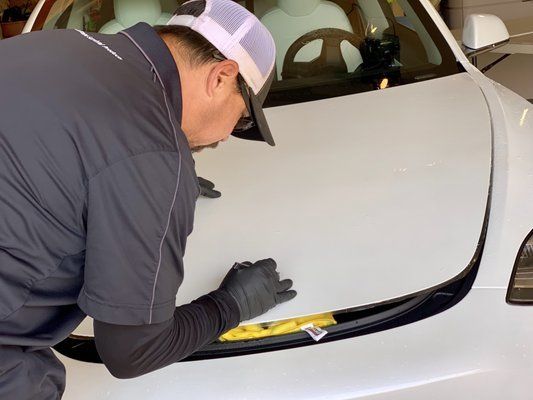 A man is working on the hood of a white car.