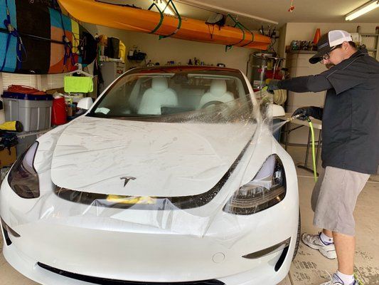A man is washing a white tesla model 3 in a garage.