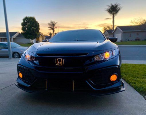 A black honda civic is parked in a driveway at sunset.