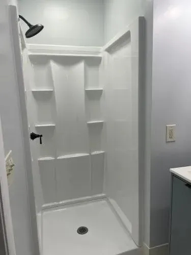White tiled shower stall with built-in shelves, showerhead, and drain in a bathroom