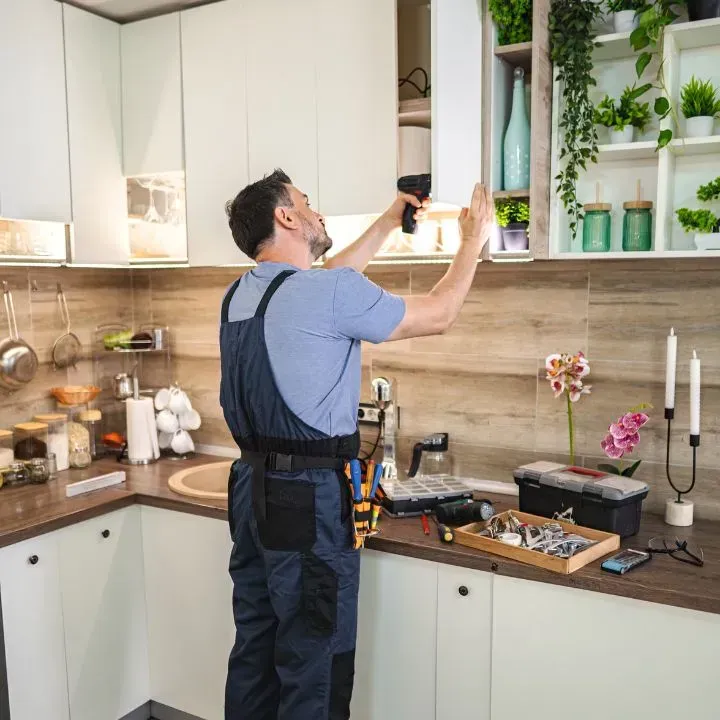 Man in work overalls installing cabinet in kitchen.