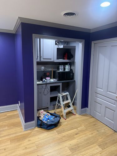 Small closet office with white cabinets, a step ladder, and tools in a purple room.