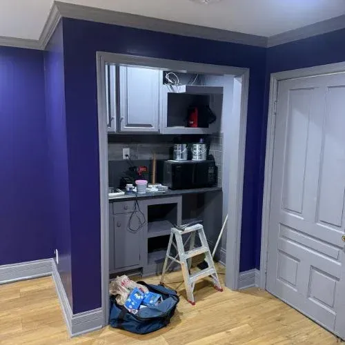 Small kitchen nook under renovation with cabinets, countertop, step stool, and tools against a purple wall