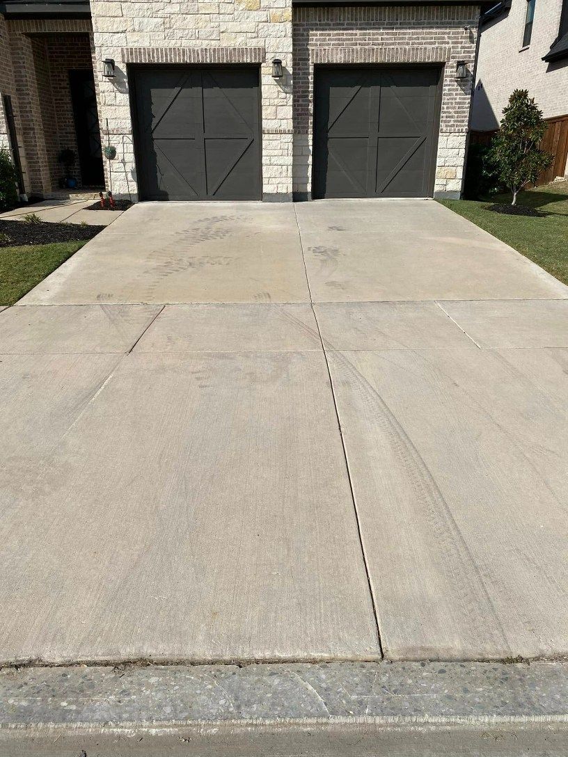 Concrete driveway leading to a two-car garage with dark gray doors. Grass and a house are visible.