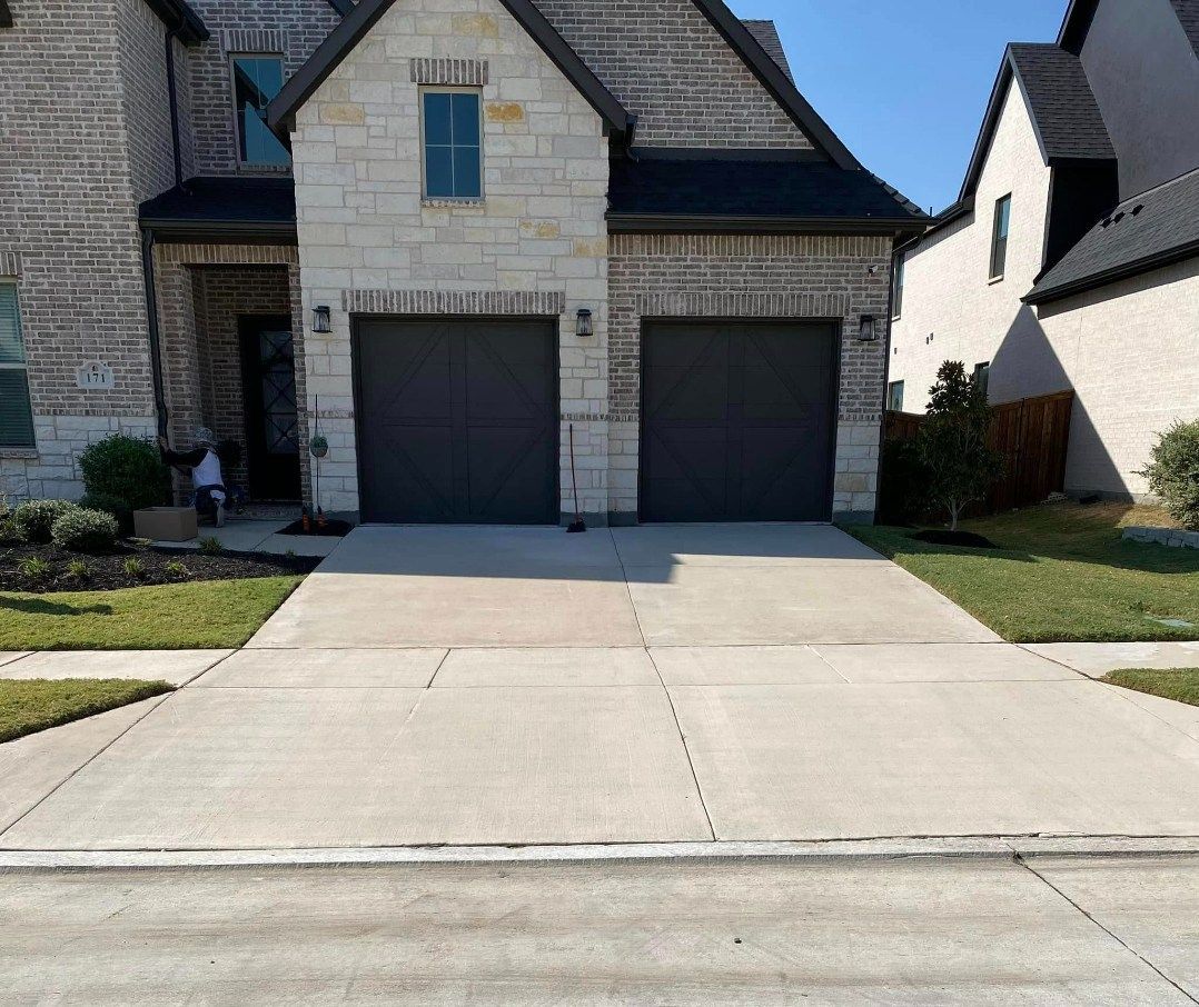 Two-car garage with gray doors on a tan brick house. A concrete driveway leads up to it.