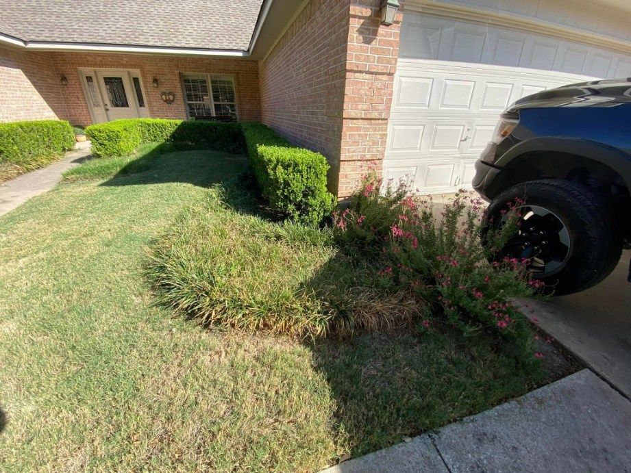 Lawn and landscaping in front of a brick house. A black truck is parked in the driveway.