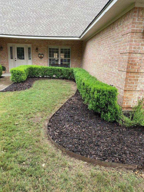 Green manicured hedge in front of a brick house with a brown mulch border.