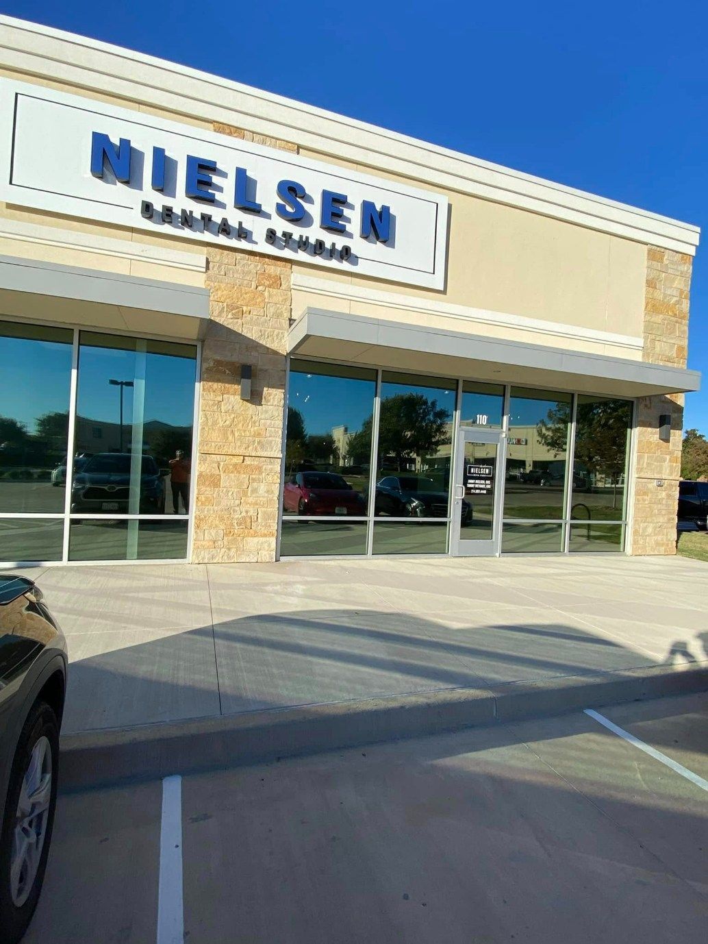 Nielsen Dental office exterior with large windows, light tan walls, and a blue sign under a clear sky.