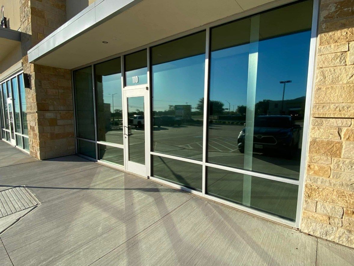 Exterior of a building with glass windows and a door reflecting the sky and a parking lot.