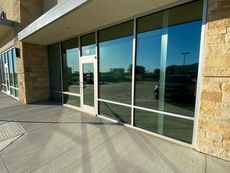 Exterior of a building with tinted windows, a door, and a stone facade, reflecting the outdoors.