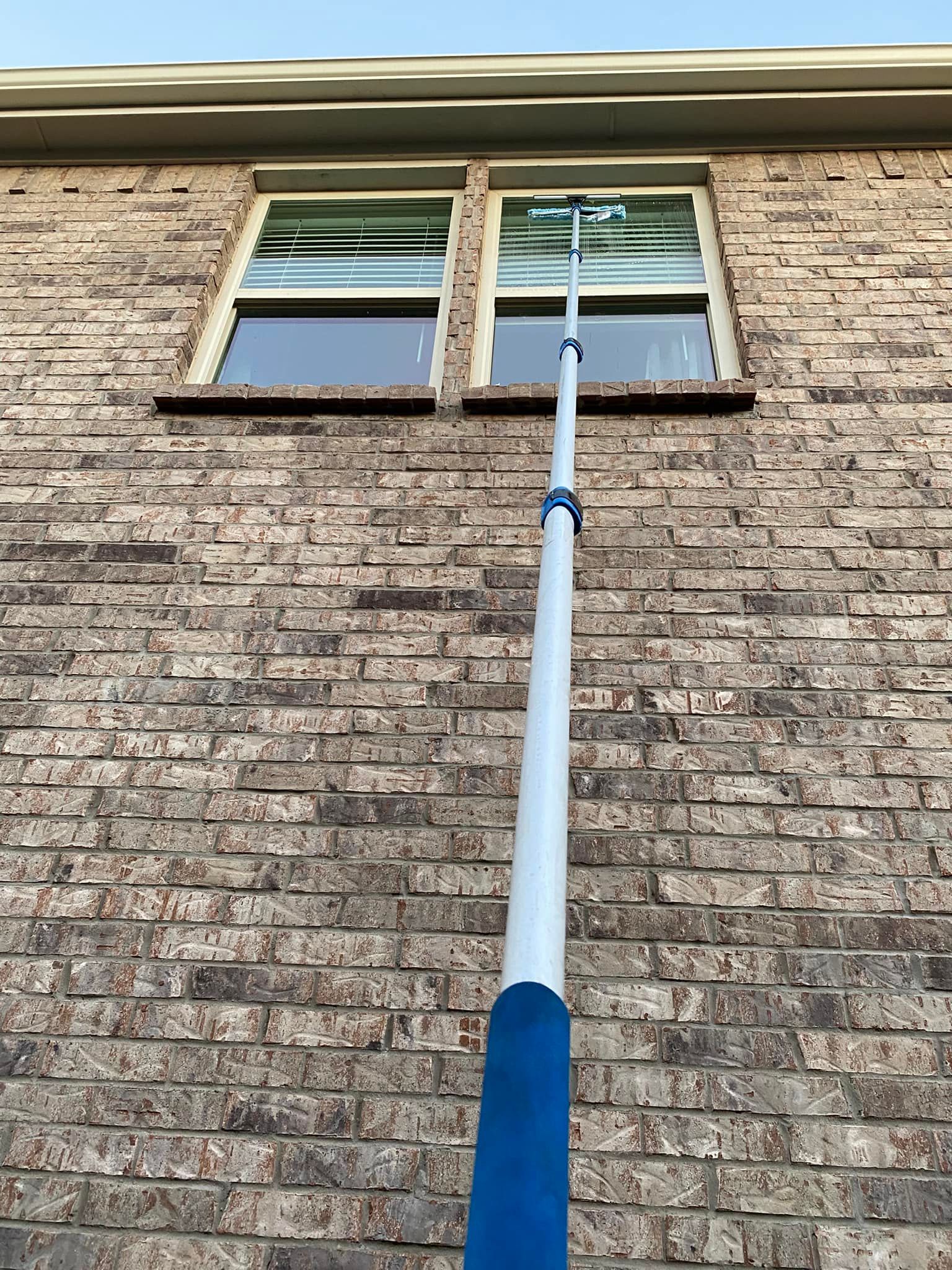 A person using a long-handled tool to clean a window on a brick building.