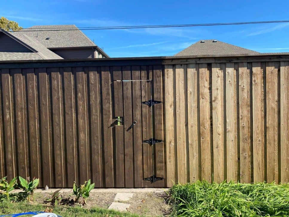 Fence, half-stained dark brown, half-unstained light brown. Shows the before and after effect of staining.