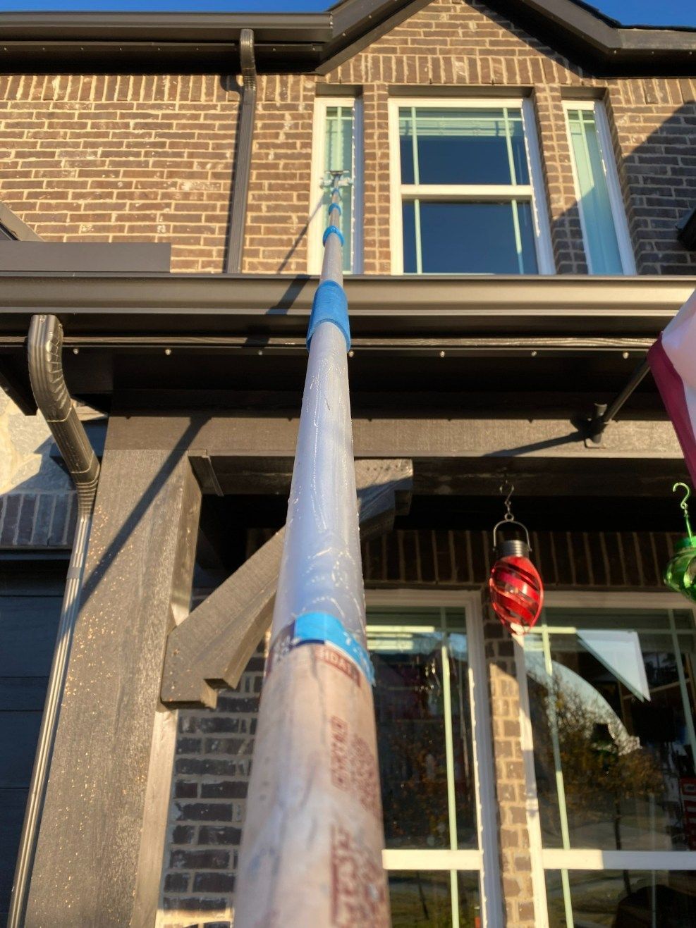 A long pole with a brush cleans a window on a two-story brick house.