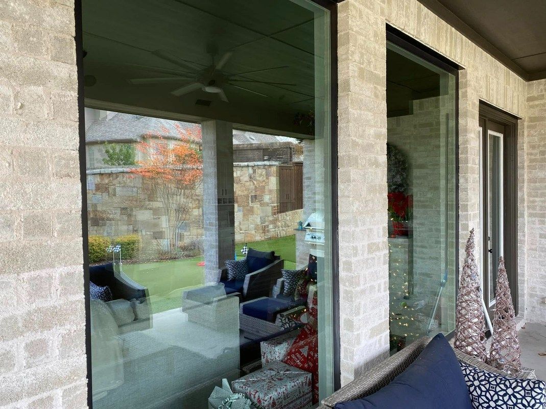 Glass doors reflecting a patio with furniture, lawn, and brick exterior.