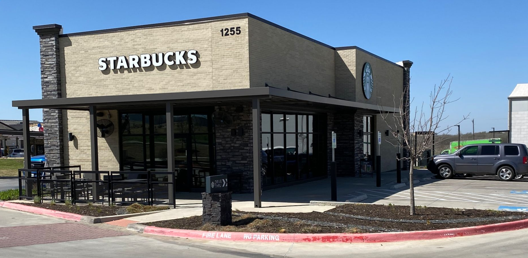 Starbucks exterior with a covered patio, a car parked nearby, and a blue sky.