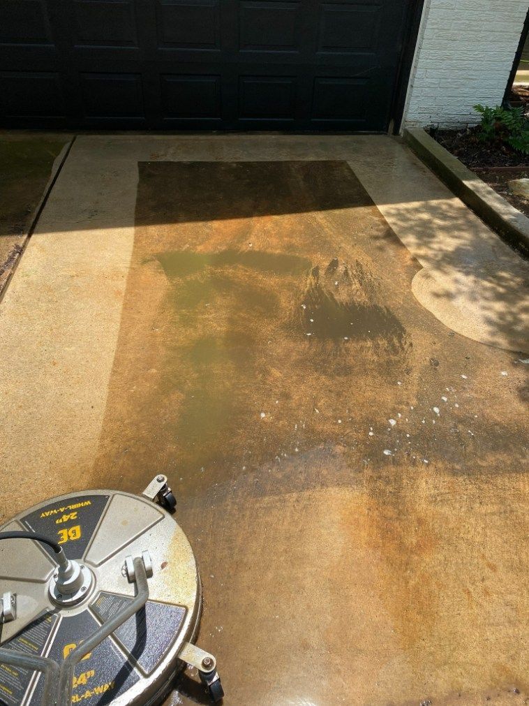 Pressure washer cleaning a concrete driveway. Sunlight, water, and circular cleaning head visible.