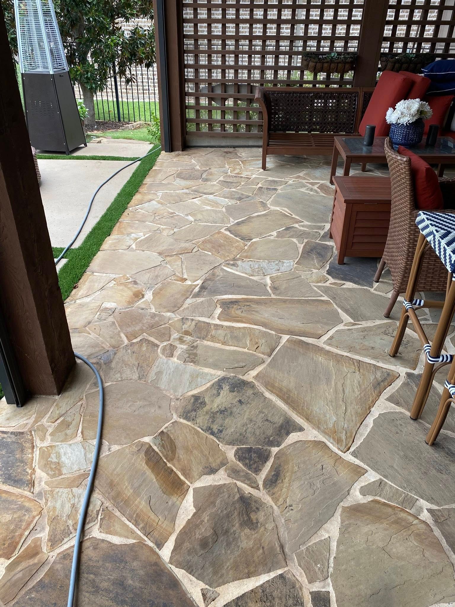Flagstone patio with outdoor furniture, edged by green grass and a dark brown wooden structure.