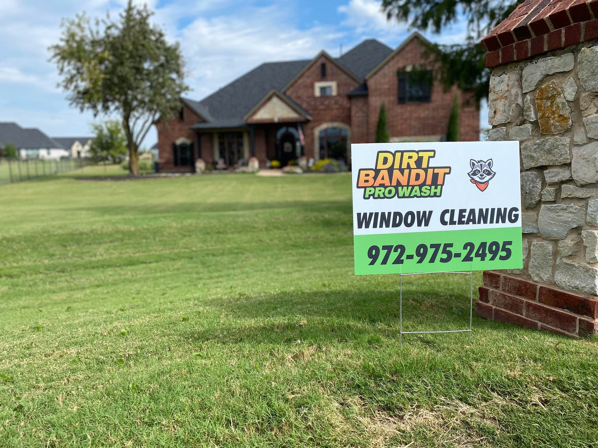 Dirt Bandit Pro Wash sign in front of a brick house, offering window cleaning services, with a phone number.