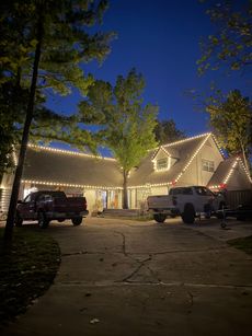 House lit with Christmas lights; two trucks parked in driveway at dusk.